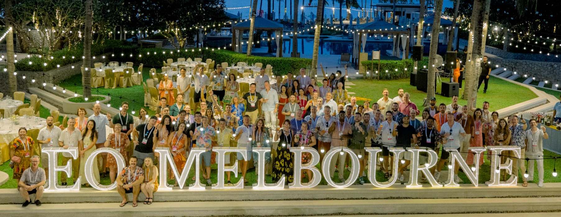 The EO Melbourne retreat group gathered behind the illuminated EO Melbourne letters at dusk in Phuket